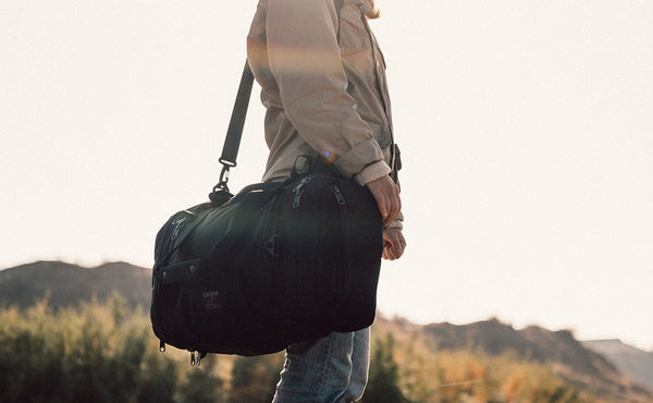 A person carrying the Road Buddy Duffel 60 via the included Shoulder Strap.